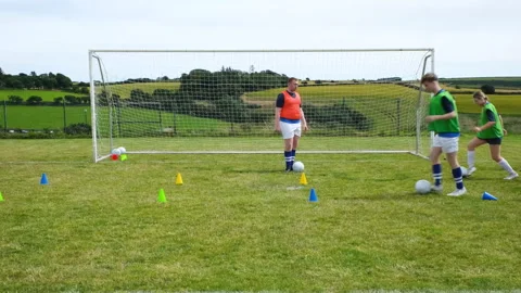 Soccer players practicing drills on field with cones and goal in background Stock Footage 310132994