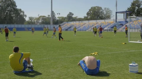 Soccer team training while two players sit in foreground 動画素材 71731596