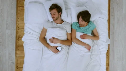 Social problem. Girlfriend taking smartphone of his boyfriend, while he is sleep Stock Footage 85664562