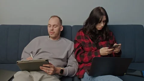 Social trend. Couple sharing time together with gadgets sitting in home interior Stock Footage 283851560