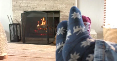 Socked feet resting on coffee table relaxing as embers dancing behind fireplace Stock Footage 340256889