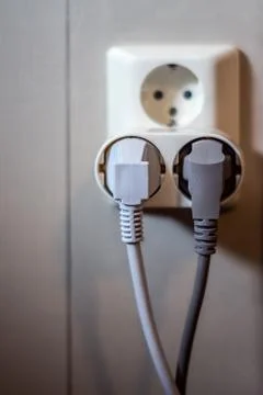 Socket on wall with two pluged electrical outlets and powercords Stock Photos