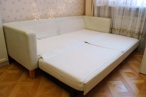 Sofa is opened to reveal space for sleeping in room with curtains Stock Photos