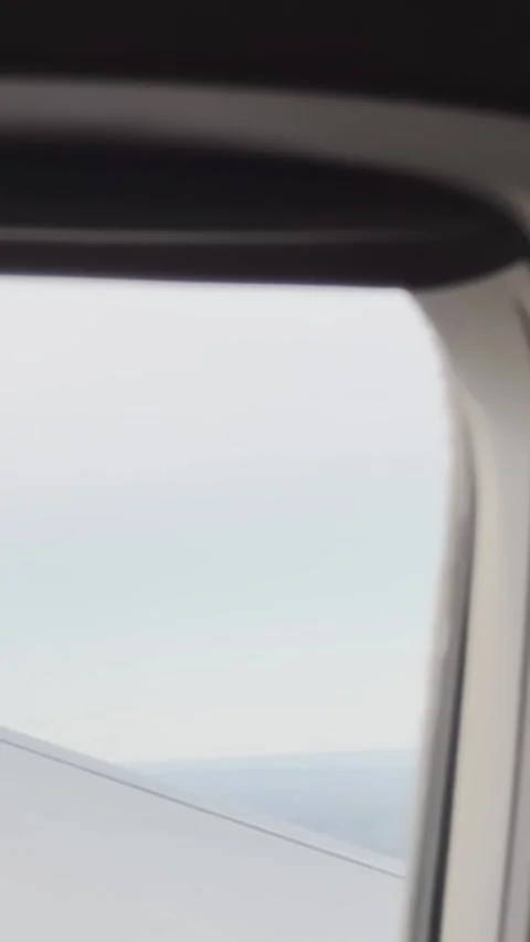 Soft airplane window view with pale wing edge, hazy sky and distant coastline Stock Footage 337229052