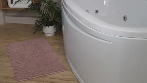 Soft bath mat near tub on wooden floor in bathroom Stock Photos