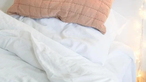 Soft bedding with white sheets and a textured pillow on a cozy bed Stock Photos