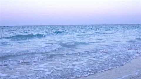 Soft blue ocean waves edged in white foam glide gently onto golden sand as sky Stock Photos
