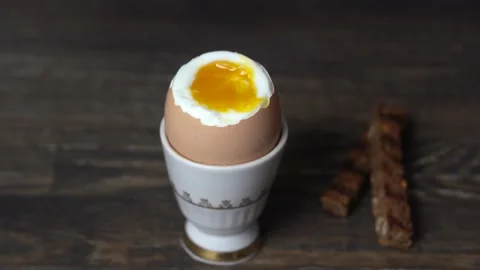Soft boiled brown egg in eggcup on wooden table background. Close up Stock Footage 139489134