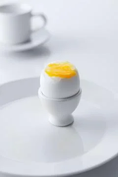 Soft boiled egg in egg cup on white background, plate and cup. Close up. Sele Stock Photos