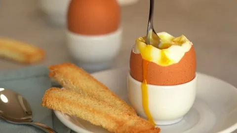 Soft-boiled egg on plate with fresh toast bread. Close up of spoon scoops up Stock Footage 160493735