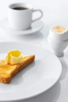 Soft boiled egg, toasted bread, butter and cup of coffee on white table. Sele Stock Photos