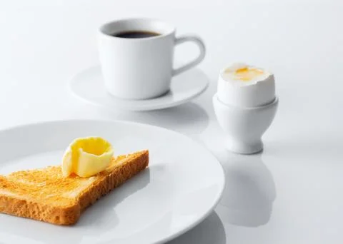Soft boiled egg, toasted bread, butter and cup of coffee on white table. Sele Stock Photos