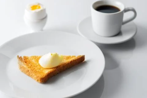 Soft boiled egg, toasted bread, butter and cup of coffee on white table. Sele Stock Photos