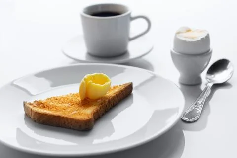 Soft boiled egg, toasted bread, butter,  cup of coffee and spoon on white tab Stock Photos