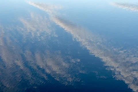 Soft cloud reflections on deep blue water surface 库存照片
