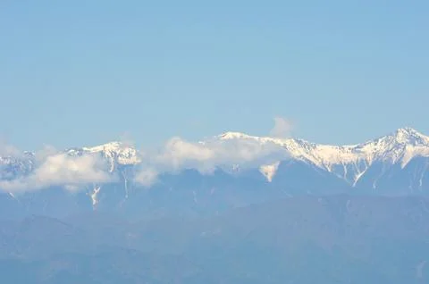 Soft clouds below the top of snow covered mountains, with a blue sky. Stock Photos