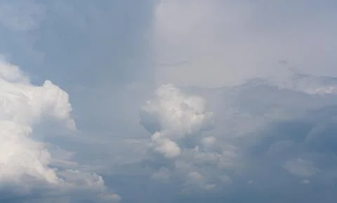 Soft clouds drift above a calm, pale blue sky Stock Photos
