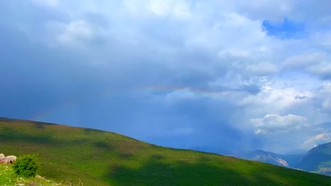 Soft cloudy sky with faint rainbow above green hill landscape Stock Footage 310246321