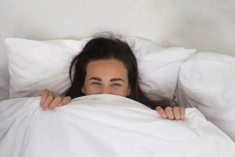In soft cocoon of her bed, a contented woman wears a morning smile, hiding Foto stock