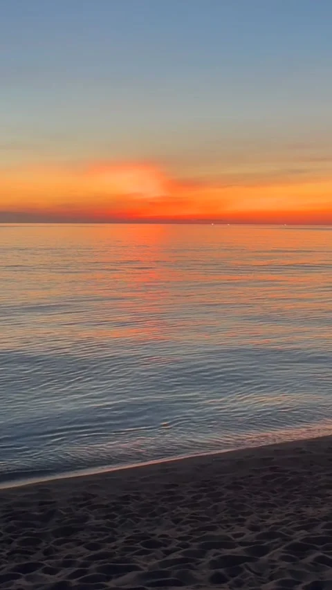 Soft dawn colors spread across calm sea and quiet sandy beach. Gentle ripples Stock Footage 339897448