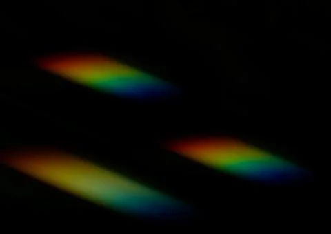 Soft diagonal streaks of rainbow light glow against a deep black background.. Photos