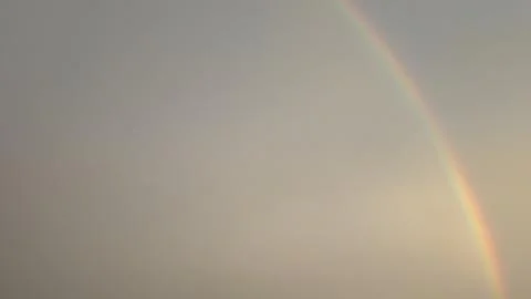 A soft, diffused sky features a single, clear rainbow segment. Muted gray, .. Stock Photos
