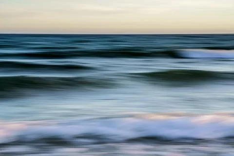 Soft, flowing ocean waves captured in a blur during sunset. Stock Photos