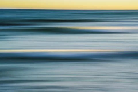 Soft, flowing ocean waves captured in a blur during sunset. Stock Photos