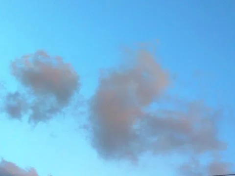 Soft fluffy clouds in a clear blue sky during sunset or dusk Stock Photos