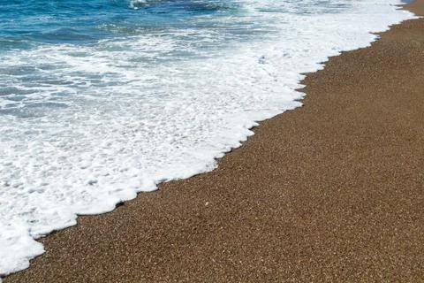 Soft, foamy waves break upon the sandy beach Stock Photos