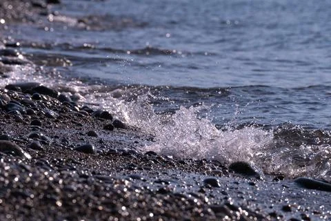 Soft foamy waves roll on the pebble sea beach Stock Photos