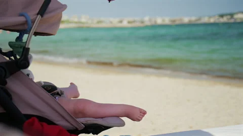 Soft focus beach scene with a baby's feet resting in a stroller, with sandy Stock Footage 339759312