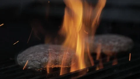 Soft Focus Flipping Two Tall Meat Burgers on a Fire Grill Stock Footage 128759247