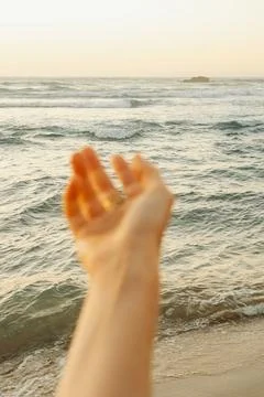 Soft focus. Reaching hand towards the ocean waves at sunset on a sandy beach. Stock Photos