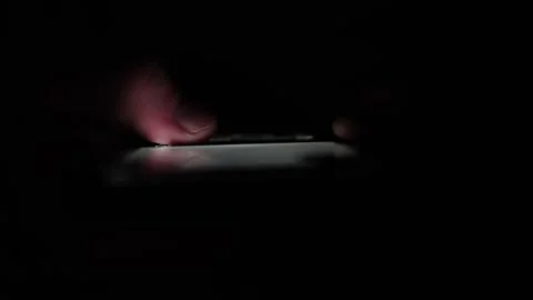 Soft glow of smartphone screen lights up fingertips in total darkness creating a Stock Footage 313842849