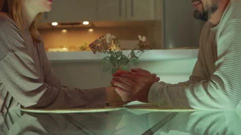 Soft-glowing light highlighting couple's intertwined hands resting on glass.. Video stock 304053200