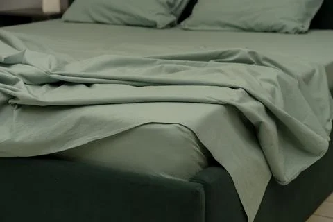 Soft green bedding on modern bed with rumpled sheets and pillows Stock Photos