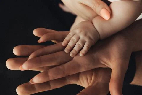 Soft hands cradle a tiny baby's hand 스톡 사진