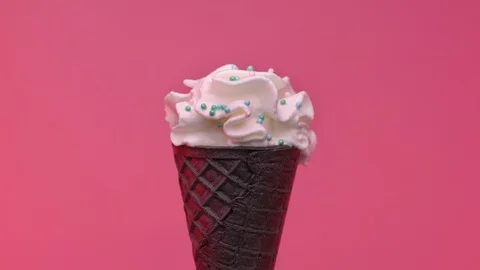 Soft ice cream in black cone decorated with colorful sprinkles over pink Stock Footage 108801035