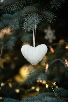 A soft knitted heart hangs on the branches of a decorated Christmas tree on t Stock Photos