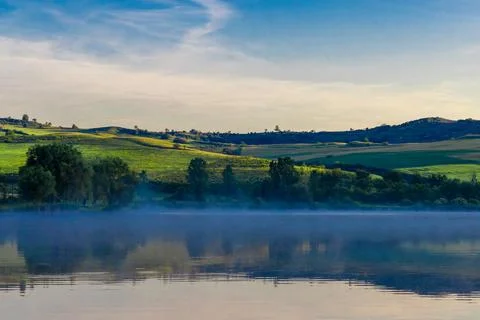 A soft layer of low-lying fog drifts over the calm water surface Foto stock