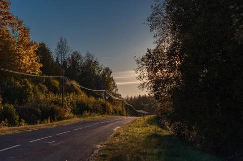 Soft light of the setting evening sun reflects on power lines along an asph.. Stock Photos