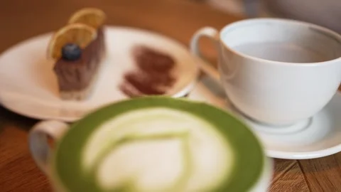 Soft matcha latte forming delicate heart pattern beside rich chocolate cake Stock Footage 303882571