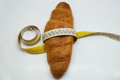 Soft measuring ruler wrapped around a croissant as a symbol of unhealthy nutr Foto stock