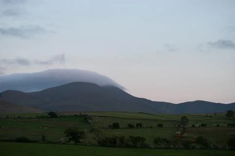 Soft Mist Clouds Drift Over a Mountain at Sunset Above Rolling Pastures Stock Photos