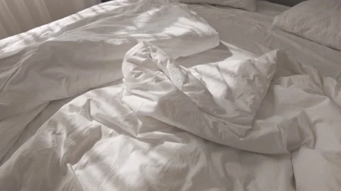 Soft morning sunlight casting shadows on wrinkled white cotton bedsheets 스톡 동영상 313256172