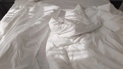 Soft morning sunlight casting shadows on wrinkled white cotton bedsheets 스톡 동영상 313256337