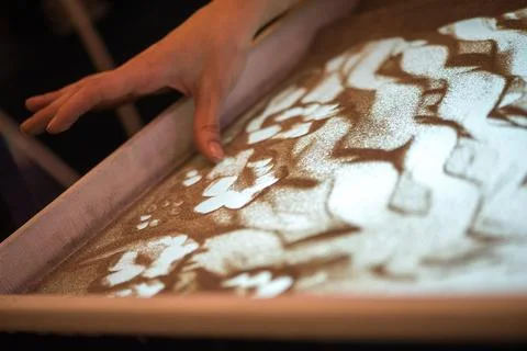 Soft Motion Of Hands Creating Abstract Shapes In Illuminated Sand Surface Sce 库存照片