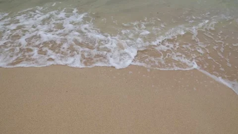 Soft ocean wave with white foam on a golden sandy beach.Close-up of a gentle sea Stock Footage 313783890