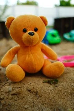 A soft orange teddy bear is placed in a sandbox with vibrant plastic toys s.. Stock Photos